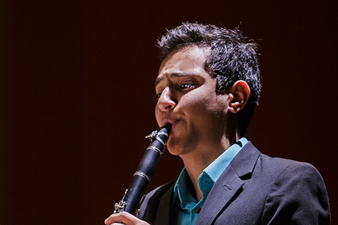 Man with dark hair in a dark suit plays the clarinet