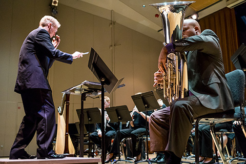 A tuba player performs with an orchestra as a director gestures with a baton