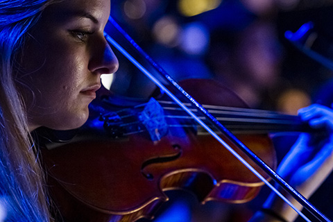 A woman under blue light plays the violin