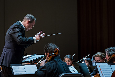 A conductor with a baton is guiding an orchestra during a performance