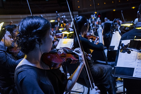 A woman with dark hair plays the violin along with the other musicians during a performance